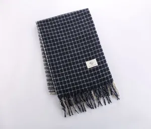 Close-up detail shot of the soft navy blue plaid scarf featuring chic fringe and brand label.