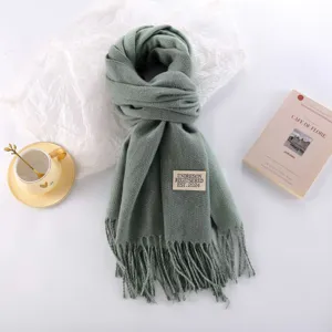 Thickened green cashmere-like winter scarf detail view, featuring fringe hem and brand label.