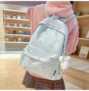 Detail view of light blue aesthetic school backpack with cute embroidery and fluffy bear pendant.