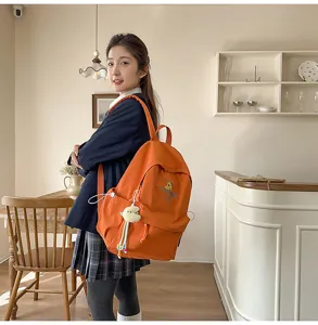Orange student backpack detail with cute plush dinosaur pendant and front embroidery.