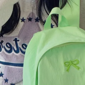 Light green canvas school backpack detail showing front zipper pocket and cute bow embroidery.