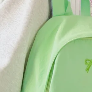 Detail view of a light green college style backpack with a cute bow embroidery.