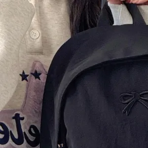 Close-up detail of the black canvas backpack featuring cute bow embroidery and student style design.