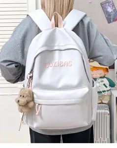 Detail shot of white casual canvas backpack with cute bear pendant and embroidered logo text.