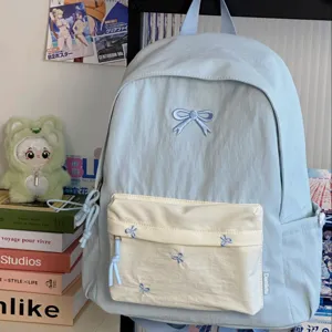 Preppy style light blue school backpack with cute bow embroidery and cream front pocket details.