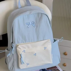 Light blue school backpack with cute bow embroidery and white front pocket for daily casual use.