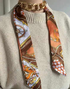 Detailed view of a fashionable narrow silk scarf and chunky chain necklace, chic style.