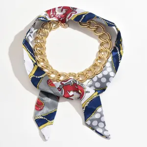 Close-up detail of a fashion chunky gold chain intertwined with a chic printed silk scarf necklace.