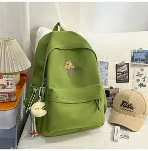 Detailed view of green canvas backpack with cartoon print, showing texture and hanging plush.