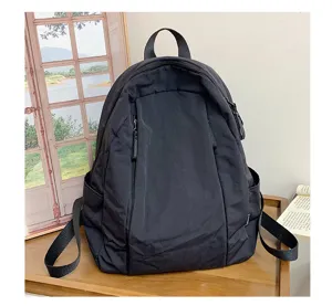 Detail view of a minimalist black casual backpack with front pocket and side compartments.