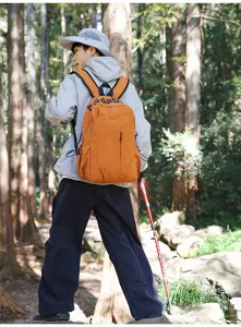 Detailed outdoor view of the orange travel backpack worn by a model in a forest setting.