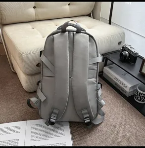 Detail view of a grey multi-strap backpack on carpet in a lifestyle setting, showing back straps.