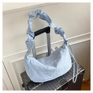 Light blue nylon pleated shoulder bag detail, casual hobo dumpling bag hanging on luggage.