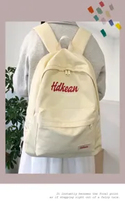 Canvas college style backpack detail showing minimalist beige design with letter print and straps.