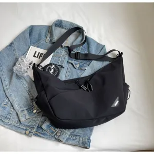Close-up of black streetwear crossbody bag with zipper, adjustable strap, and triangular logo.