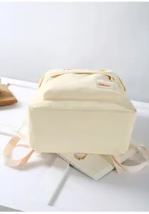 Canvas backpack detail showing front zipper pocket and fabric label in soft beige color.