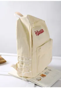 Side detail shot of a beige college style canvas backpack featuring front pocket and side cords.