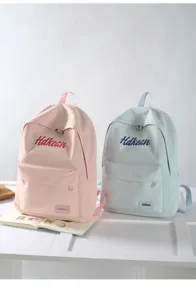 Details of casual student backpacks in pink and light blue with front zipper pockets.