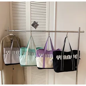 Dettaglio in primo piano di grandi borse tote in tela appese con design color block.