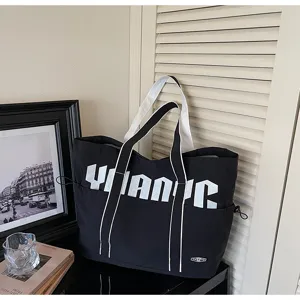 Vista dettagliata di grande borsa tote in tela con cinturini a contrasto e stampa per uso quotidiano.