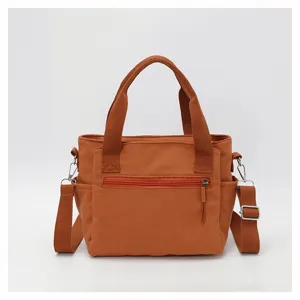 Close-up detail view of the orange nylon shoulder bag showing front zipper pocket and strap.