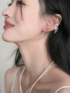 Gros plan de detail de la manchette d'oreille noeud ruban argente mat portee sur le cartilage.