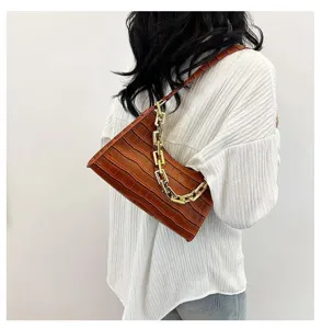 Detailed shot of trendy brown crocodile pattern baguette shoulder bag with chunky gold chain.