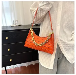 Close-up view of the chic orange crocodile pattern and bold gold chain on this trendy bag.