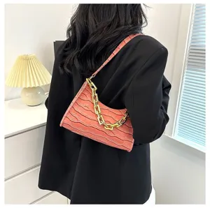 Detail shot of a pink crocodile texture baguette shoulder bag with chunky gold chain.