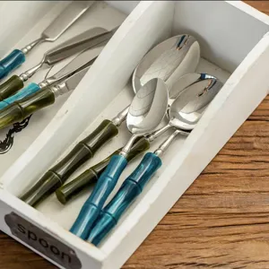 Stainless steel cutlery set with creative bamboo handle design in white storage tray detail view.