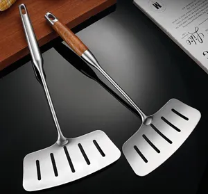 Stainless steel slotted spatula with wood handle for flipping fish and steak in kitchen cooking.