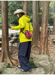 Detail shot of a red plaid crossbody phone bag worn in a natural forest outdoor setting.
