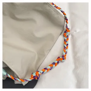 Dettaglio in primo piano della tracolla intrecciata colorata della borsa in nylon beige.