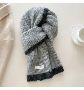 Detailed view of the gray knitted wool scarf with contrasting dark trim and woven tag texture.