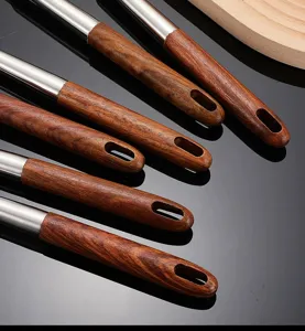Close-up detail of stainless steel kitchen utensil handle with wooden grip and hanging hole.