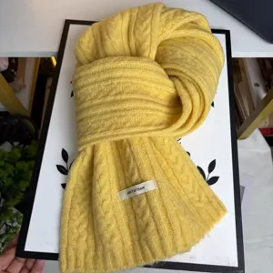 Close-up detail of a cozy yellow cable knit wool blend winter scarf with brand tag.