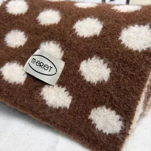 Close-up detail of cozy brown knitted winter scarf with soft white polka dots and texture.