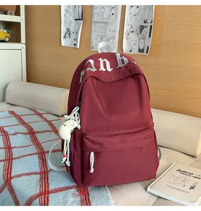 Vista dettagliata dell'elegante zaino scolastico in tela rossa con grazioso ciondolo e ricamo.