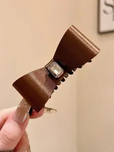 Brown satin bow hair claw clip detail, featuring a sparkling crystal rhinestone accent and secure grip teeth.