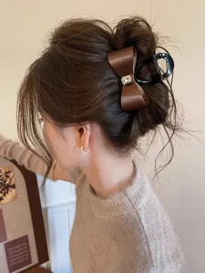 Detail shot of a brown satin bow hair claw with a sparkling rhinestone center for elegant updos.