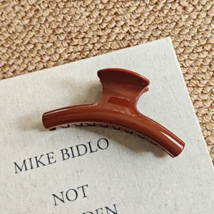 Detail view of a large brown hair claw clip on a book, showcasing the smooth glossy finish.