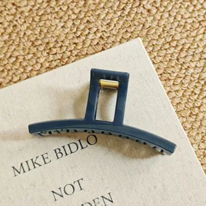Dark blue large geometric hair claw clip detail, modern minimalist shark clip accessory close up.