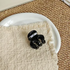 Detail close-up of a stylish black mini hair claw clip resting on a chic fabric pad.
