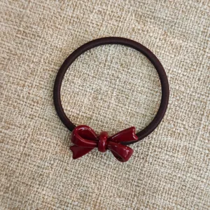 Dettaglio in primo piano dell'elastico marrone scuro con fiocco in acetato bordeaux lucido.