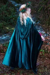 Detailed outdoor scene showcasing the dark green velvet hooded cloak in a forest setting.