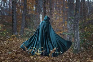 Dark green hooded cloak detail, elegant autumn forest background showcase for stage.