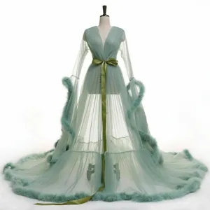 Robe longue transparente en tulle vert sauge avec bordure en plumes et ceinture en satin.