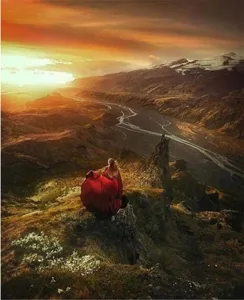 Scenic detail shot of a wine red velvet cloak worn in a majestic mountain landscape during sunset.