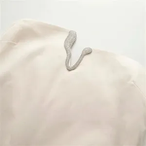Close-up of elegant rhinestone metal buckle detail on a chic beige sleeveless dress.