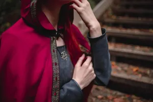 Medieval vintage style red hooded cloak cape product detail in outdoor forest scene